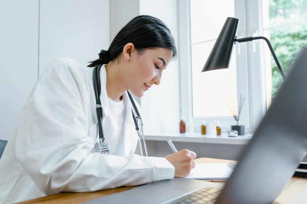Crafting Captivating Headlines: Your awesome post title goes here A female doctor writes notes at her desk with a stethoscope around her neck.